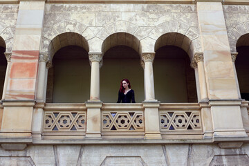 Full length portrait of red-haired woman wearing a  beautiful gothic gown costume, walking around  location with  romantic castle stone architecture background.