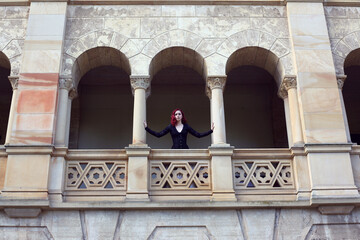 Fototapeta premium Full length portrait of red-haired woman wearing a beautiful gothic gown costume, walking around location with romantic castle stone architecture background.