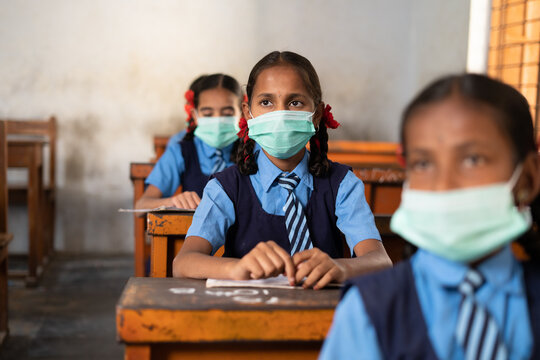 Girl kid with medical face mask listening class at school while maintaining social distance - concept of coronavirus covid-19 protection, pollution prevention and back to school