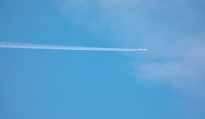 Trail of white smoke from the airplane in the blue sky