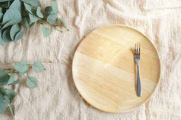 Empty round wooden dish and stainless fork placed on linen cloth in the morning light for mock up or backdrop about bakery, dessert or food with copy space. tableware setting in studio style.