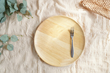 Empty round wooden dish and stainless fork placed on linen cloth in the morning light for mock up or backdrop about bakery, dessert or food with copy space. tableware setting in studio style.