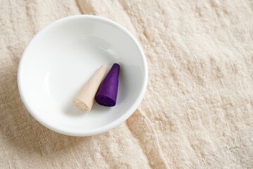 focus on white and purple incense in white dish placed on linen cloth with copy space in the morning light.