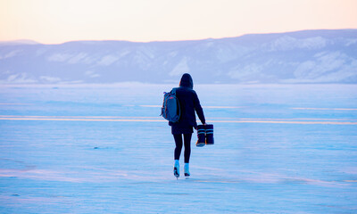 A young happy woman is skating on the transparent ice of the frozen Lake Baikal on a sunny winter...
