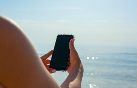 Close up photo of girls hands holding phone against the sea background. Woman taking picture of seascape on sunny day. Mock up. Copy space. Social media, modern technologies. Summertime. Blogging