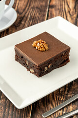 Walnut and dark chocolate brownie on a white porcelain plate on wooden table