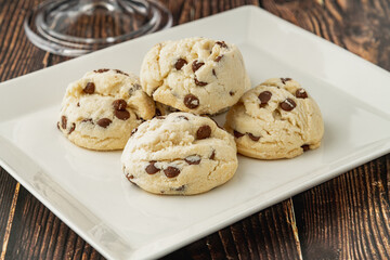 Stacked chocolate chip cookies in white plate on wooden table