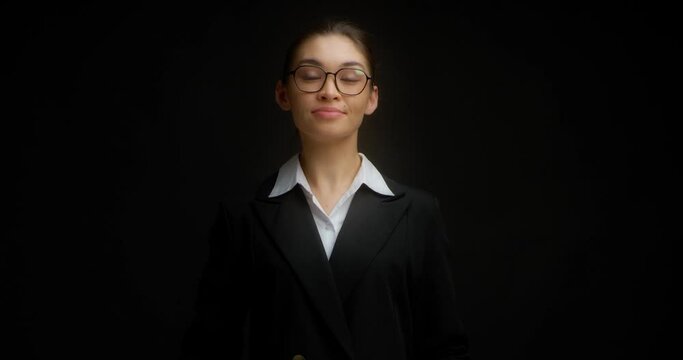 Business woman in glasses and a business suit makes a two-handed Come here gesture. Young Asian woman beckons you to come over with a beckoning gesture. Isolated on a black background