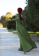 Full length portrait of red haired woman wearing a  beautiful  green medieval fantasy gown. Posing with gestural hands on a enchanted forest background.