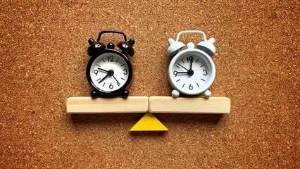 Alarm clocks on a wooden seesaw, both equally balance. 