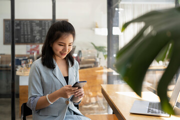 Fototapeta na wymiar Pretty young asian woman sitting in modern coffee shop and using smart phone.