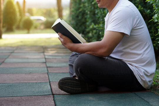 Man sits on the floor, reads book in the park. Concept : Relax time, pastime, hobby. Give time for yourself to read books , magazine, novels. Reading in daily life. Education ,knowledge or  pleasure.