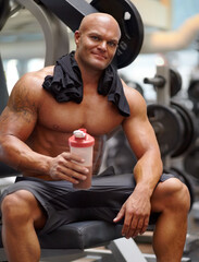 Enjoying a protein shake after a workout. Portrait of a male bodybuilder holding a protein shake while sitting on a weight bench at the gym.