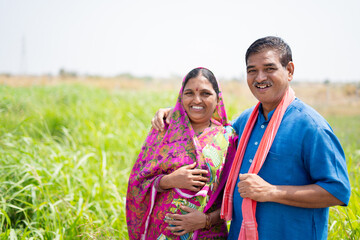 Portrait shot of smiling Indian village couple at meadow looking at camera - concept of happy family, rural lifestyle and togetherness
