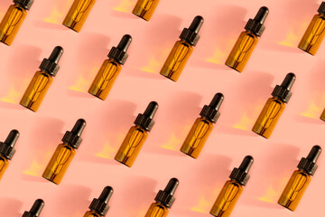 Pattern of Transparent amber green glass dropper bottles with liquid inside on beige background in the sunlight. Pipette with fluid hyaluronic acid, serum, retinol. Cosmetics, healthcare, beauty 
