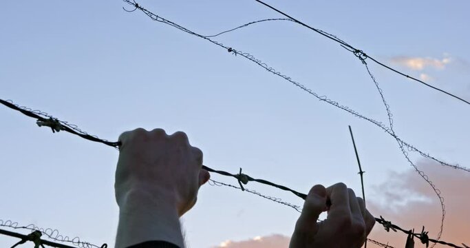 Man grabs barbed wire against clear sky