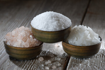 Different natural types of salt on a wooden background. Salt crystals in a wooden container