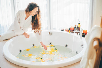 Beautiful woman relaxing at spa.Young lady in bathrobe touching water in jacuzzi. - obrazy, fototapety, plakaty