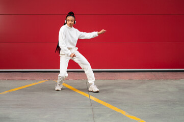 Cheerful African American woman with headphones
dancing urban dance on a red background