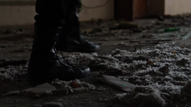 Feet wearing black shoes silhouette walking through an abandoned ruined building alone. slow motion video