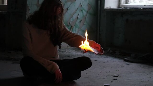 Man wearing mask sitting in abandoned building burning paper. slow motion video