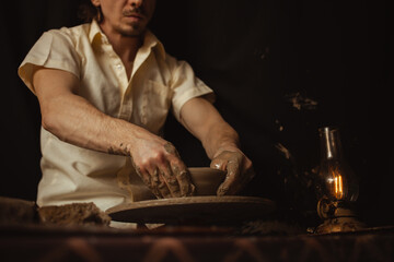man in pottery workshop makes plate of clay, an authentic atmosphere, yellow lamp, lifestyle, magical atmosphere. Concept with your own hands, home entertainment. potter's wheel