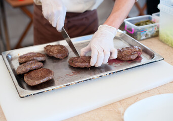 The cook in gloves cuts burger cutlets checking the readiness of meat