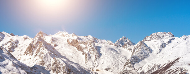 Panorama of winter snowy mountains in Caucasus region in Russia with bright sun on background
