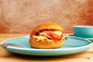 Closeup bagel with chicken, tomato and cheese on wooden table.