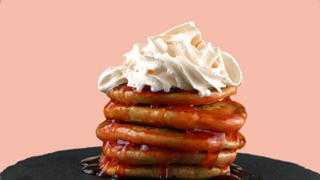 American pancakes with strawberry topping and whipped cream. On a pink background.