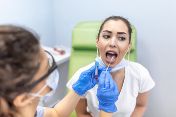 Doctor in a protective suit taking a throat and nasal swab from a patient to test for possible...