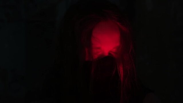young man with long hair wearing black mask on his face in the light of red candle opening his eyes, slow motion video