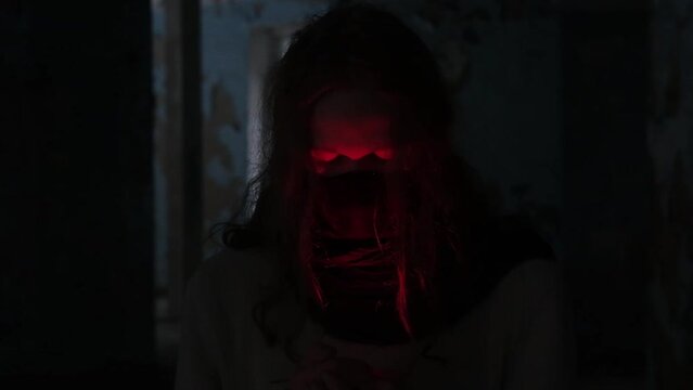 young man with long hair wearing black mask on his face in the light of red candle opening his eyes, slow motion video