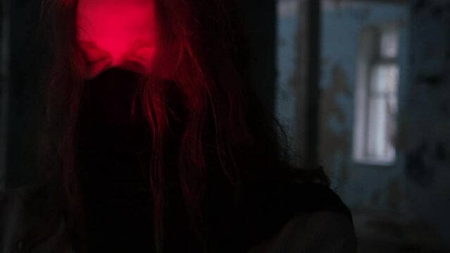 young man with long hair wearing black mask on his face in the light of red candle opening his eyes, slow motion video