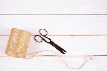 A ball of jute rope and retro scissors on a white wooden background. The concept of floristry or gardening,packaging,hobby,sewing,knitting,craft.Top view.Space for copying.