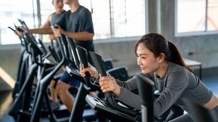 Healthy Asian athletic man and woman in sportswear workout exercise on cycling machine together at...