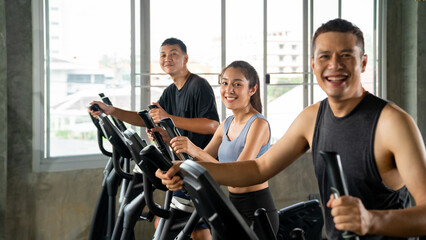 Healthy Asian athletic man and woman in sportswear workout exercise on cycling machine together at fitness gym. Wellness male and female do sport training at sport club. Health care motivation concept
