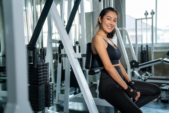 Portrait of Smiling Asian athletic woman in sportswear workout exercise with exercise machine at fitness gym. Healthy wellness female do sport training at sport club. Health care motivation concept