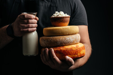 craftsmanship hands have a typical Italian cheese. French tomme cheese in the hands of a cheesemaker on dark background. Different homemade cheeses. banner, menu, recipe place for text
