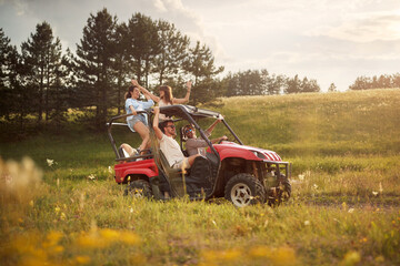 Fototapeta na wymiar Friends cheering and enjoying beautiful sunny day while driving an off road buggy car on mountain nature. Freedom, friendship, nature concept.