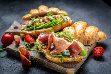 Variety of aperitifs Croissant sandwiches with jamon ham serrano paleta iberica, blue cheese, avocado, microgin on blue background. Delicious snack, appetizers, tapas