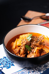 Asian Food concept Spicy beef and Kimchi Soup or stew Kimchi Jjigae in black ceramic bowl on wooden board with copy space