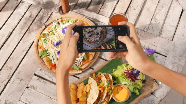 Young Blogger Woman Taking Photo of Mexican Food Using Mobile Phone in Vegan Restaurant. 4K Slowmotion Flatlay Food Porn Concept on Wooden Table View From Above. Bali, Indonesia.