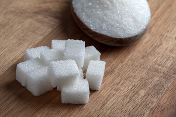Granulated sugar and sugar cubes in wooden spoon on wooden background	