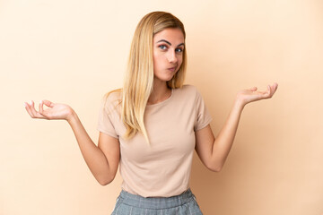 Blonde Uruguayan girl isolated on beige background having doubts while raising hands