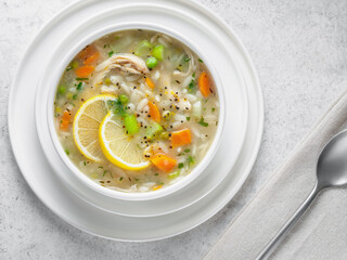 A portion of Italian lemon chicken orzo soup in white bowl. Light background. Flat lay, close-up. From above. Horizontal