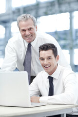 Successful web design. Portrait of a mature businessman standing behind a younger colleague while viewing a laptop.