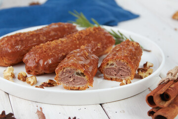 Beautiful delicious french eclairs set with original cream decor on white plate on wooden background, tasty colorful dessert profiteroles