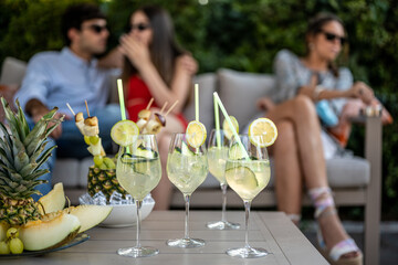 cocktails drink glasses on a table in foreground, celebration event with happy people on background, focus on fruit and beverage