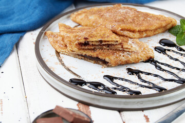Crepes stuffed on plate, thin pancakes, blini, white wooden table